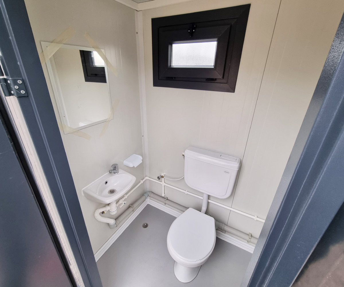 Contentor sanitário novo de formato compacto, equipado com sanita, urinol e lavatório.
